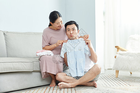 俏皮丈夫和孕妇在家收拾婴儿服饰图片