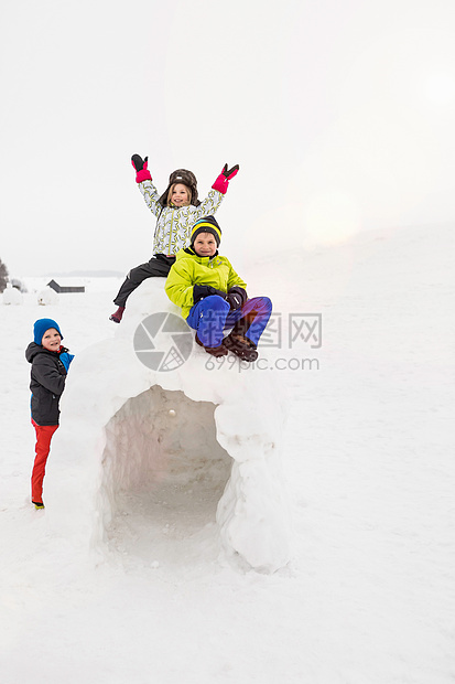 三个孩子坐在雪屋上玩耍图片