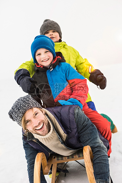 父亲和两个男孩在雪中玩雪橇图片