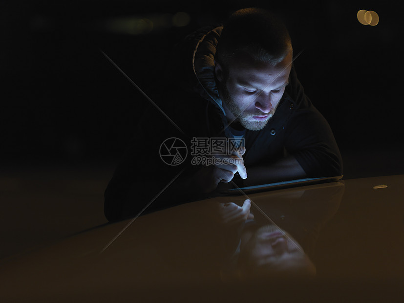 年轻人使用数字平板电脑，户外，夜间，面部照明图片
