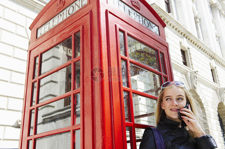 电话亭旁边的女人，在她的手机上图片