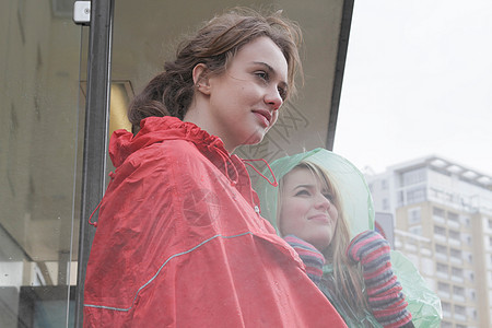 2名身穿雨衣的年轻女子在车站等车图片