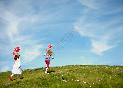 绿色草坪上拿着风车奔跑的两个小女孩图片