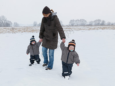 和双胞胎儿子在雪地里散步的女人图片