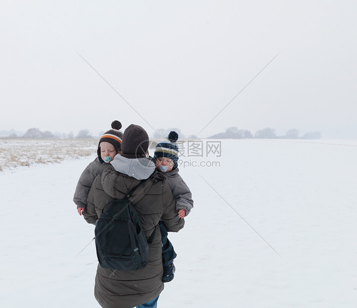 和双胞胎儿子在雪地里散步的女人图片