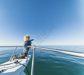 男孩跪在船上，帆船的船头朝一边看图片