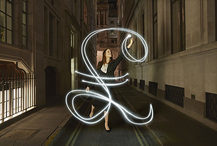 女商人在晚上城市街道上画发光的英镑标志图片