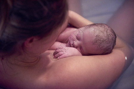 在家里的婴儿池里抱着新生婴儿的年轻妇女图片