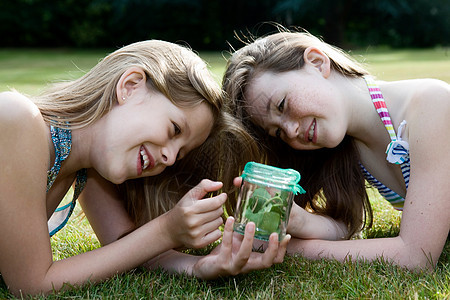 两个女孩看着有昆虫的罐子图片
