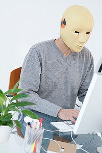 戴着撞车假面具的人在电脑前工作图片