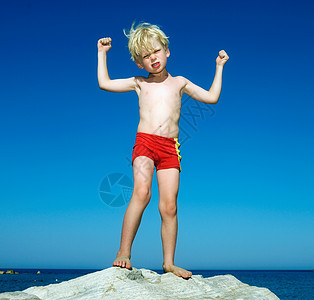 小男孩站在水边的大石头上背景图片