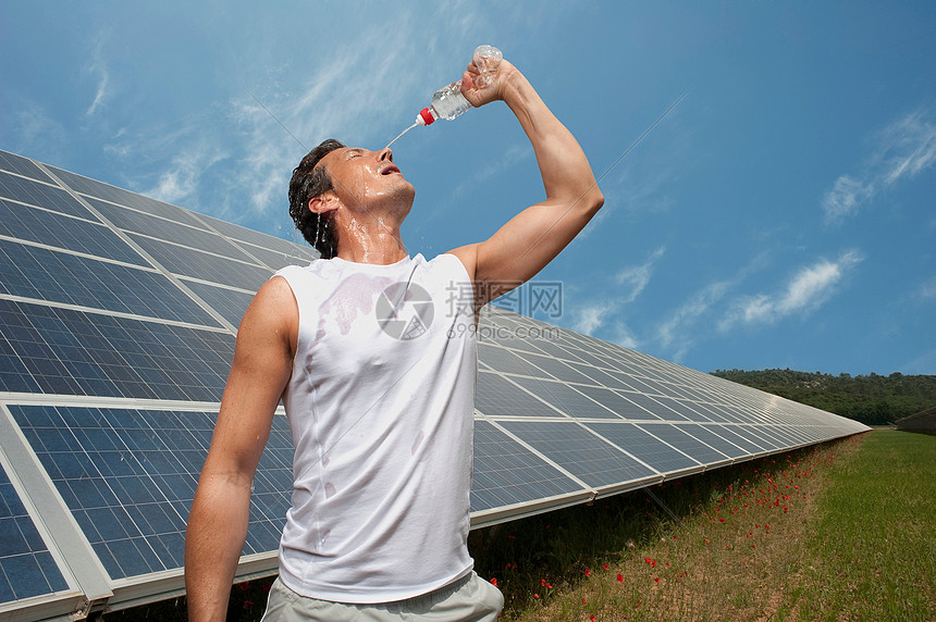 在太阳能板前喝水的男人图片
