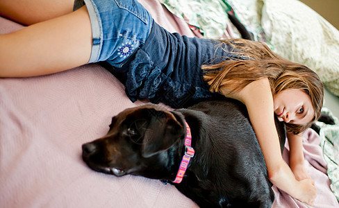 女孩躺在床上和狗一起放松图片