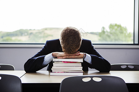十几岁的男生低着头坐在书桌旁图片素材