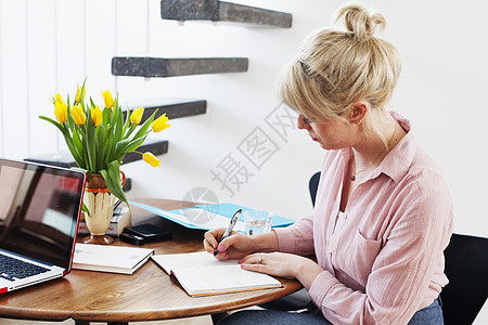 坐在桌旁写字的年轻女子图片