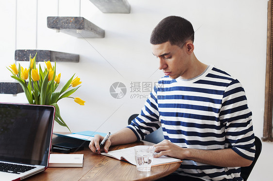 年轻人坐在桌旁，写在笔记本上图片