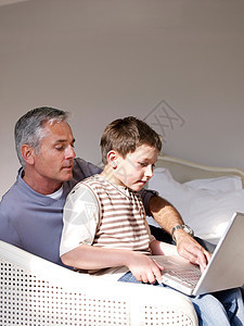父亲和儿子在卧室使用笔记本电脑图片