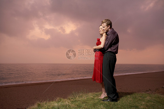 日落时分站在海滩边的一对夫妇图片