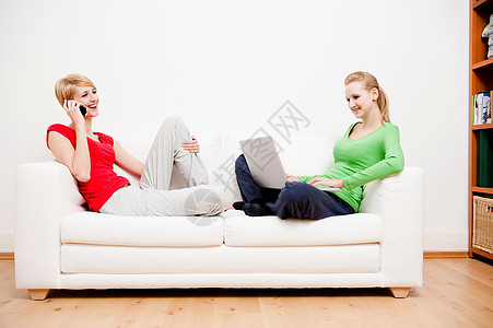 两个女人在沙发上用笔记本和打电话图片