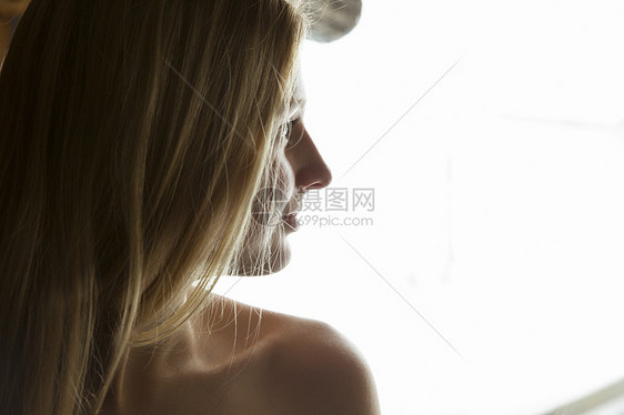 从桑拿窗口凝视的光肩膀年轻女子的肖像图片