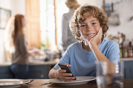 十几岁的男孩在餐桌上拿着智能手机图片