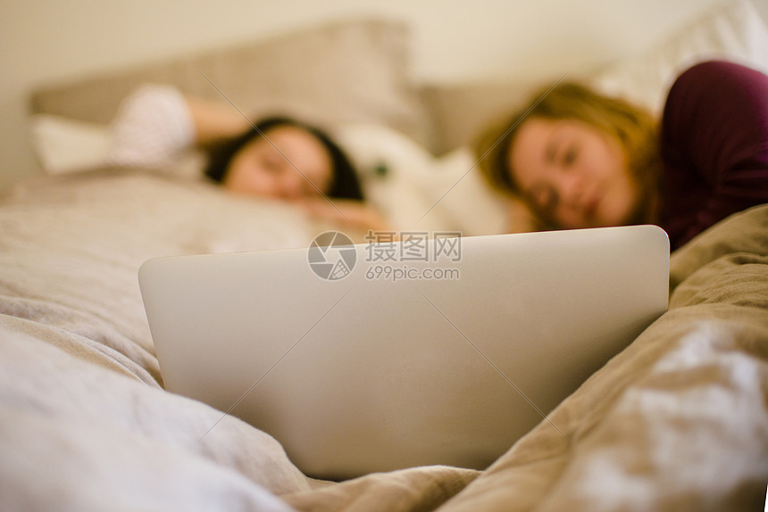 两个年轻的女性朋友躺在床上看笔记本电脑图片
