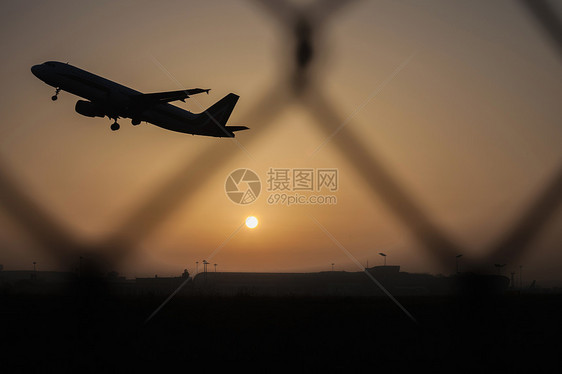 日落时分起飞的飞机，透过铁丝网看去图片