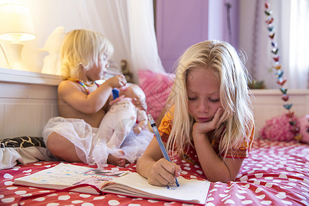 女孩和学步的妹妹躺在床上玩彩色书图片