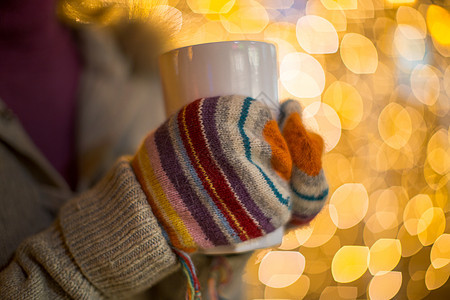 女生手戴手套在圣诞灯前拿着热饮料的特写镜头图片
