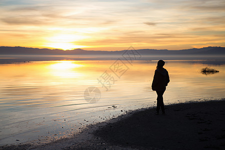 年轻女子站在水边，看日落图片