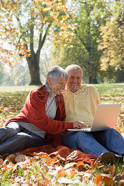 在公园里用笔记本电脑的老年夫妇图片