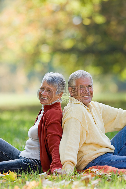 背靠背地坐在公园里的老年夫妇图片