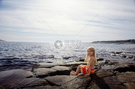坐在湖边岩石上的男孩图片