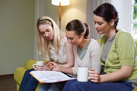 三个年轻女人坐在沙发上喝水看书图片
