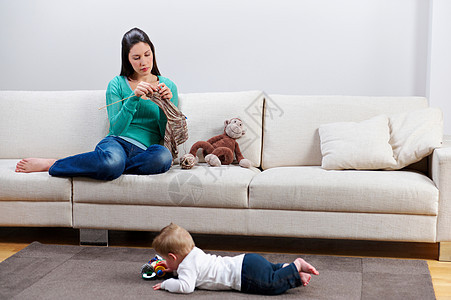 妇女边编织看着婴儿在地板上玩耍图片