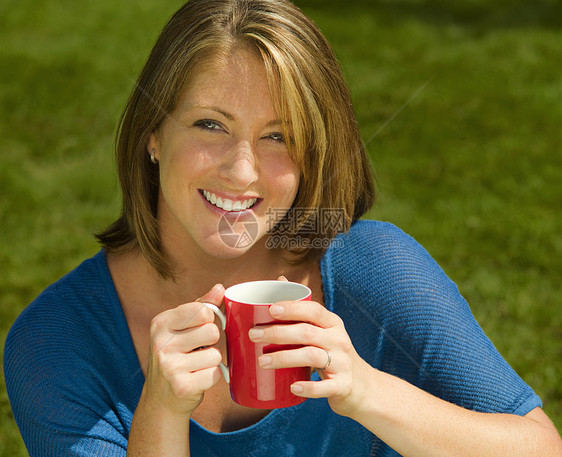 在草坪上喝热饮料的女人图片