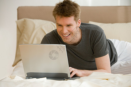 在床上用笔记本电脑的男子图片