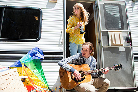 带吉他和摄像机的旅行车旁的一对年轻夫妇图片