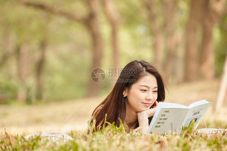 年轻女性趴在草地上看书图片