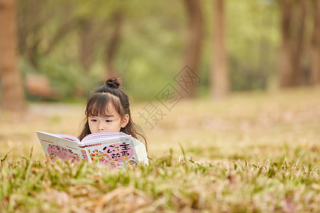 小女孩趴在草地上读童话故事图片