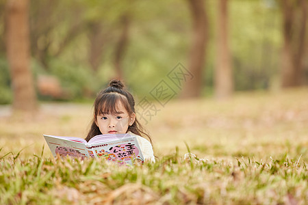 小女孩趴在草地上看童话故事图片