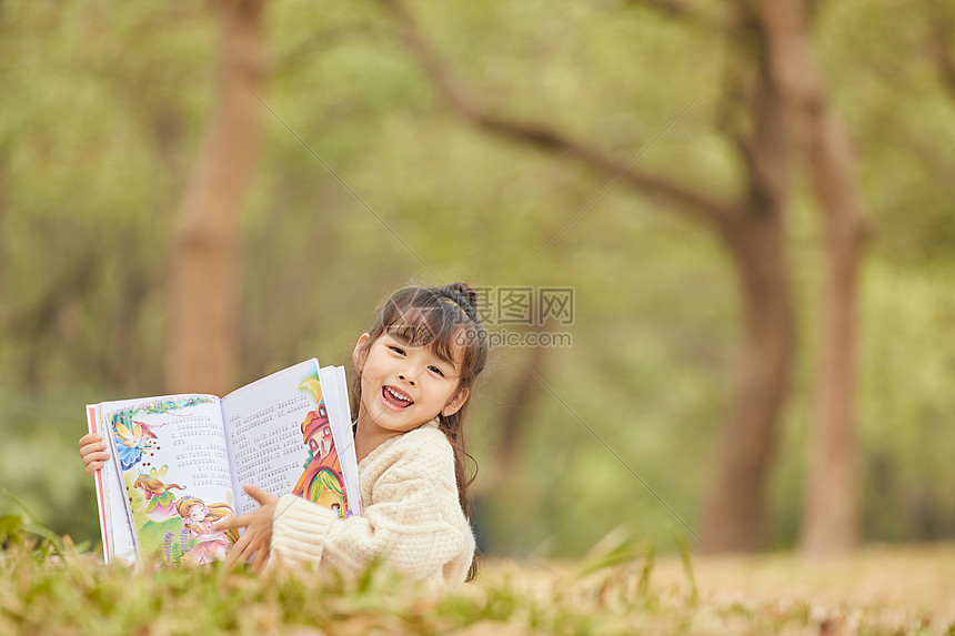 小女孩趴在草地上看童话故事图片