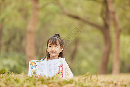 小女孩趴在草地上看童话故事图片