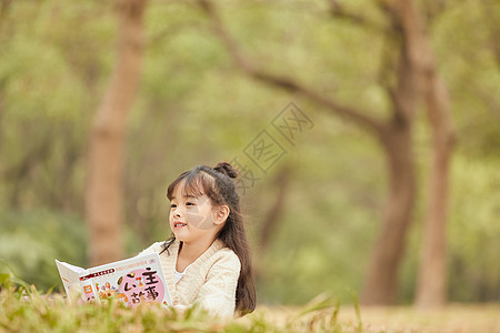 小女孩趴在草地上看童话故事图片