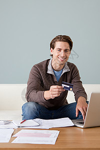 年轻人一手拿着信用卡一手触摸笔记本电脑图片
