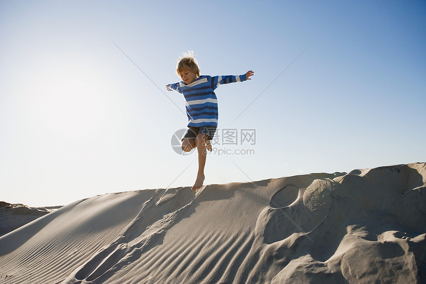 男孩在沙丘上跳跃图片