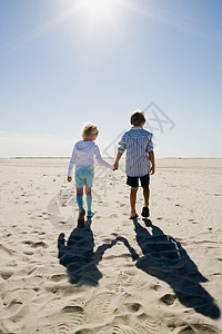 男孩和女孩手牵着手，在海滩上散步图片