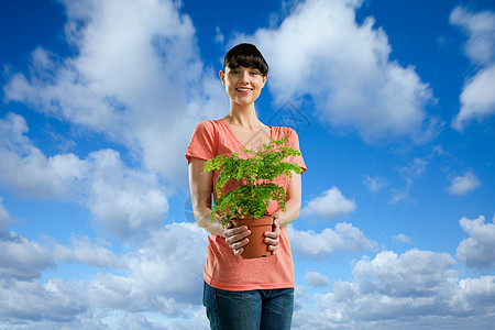 年轻的女子拿着植物在蓝天白云下图片