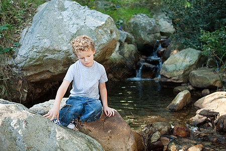 坐在河边岩石上的男孩图片