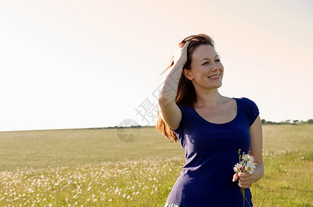 微笑的女人在草地上拿着花图片